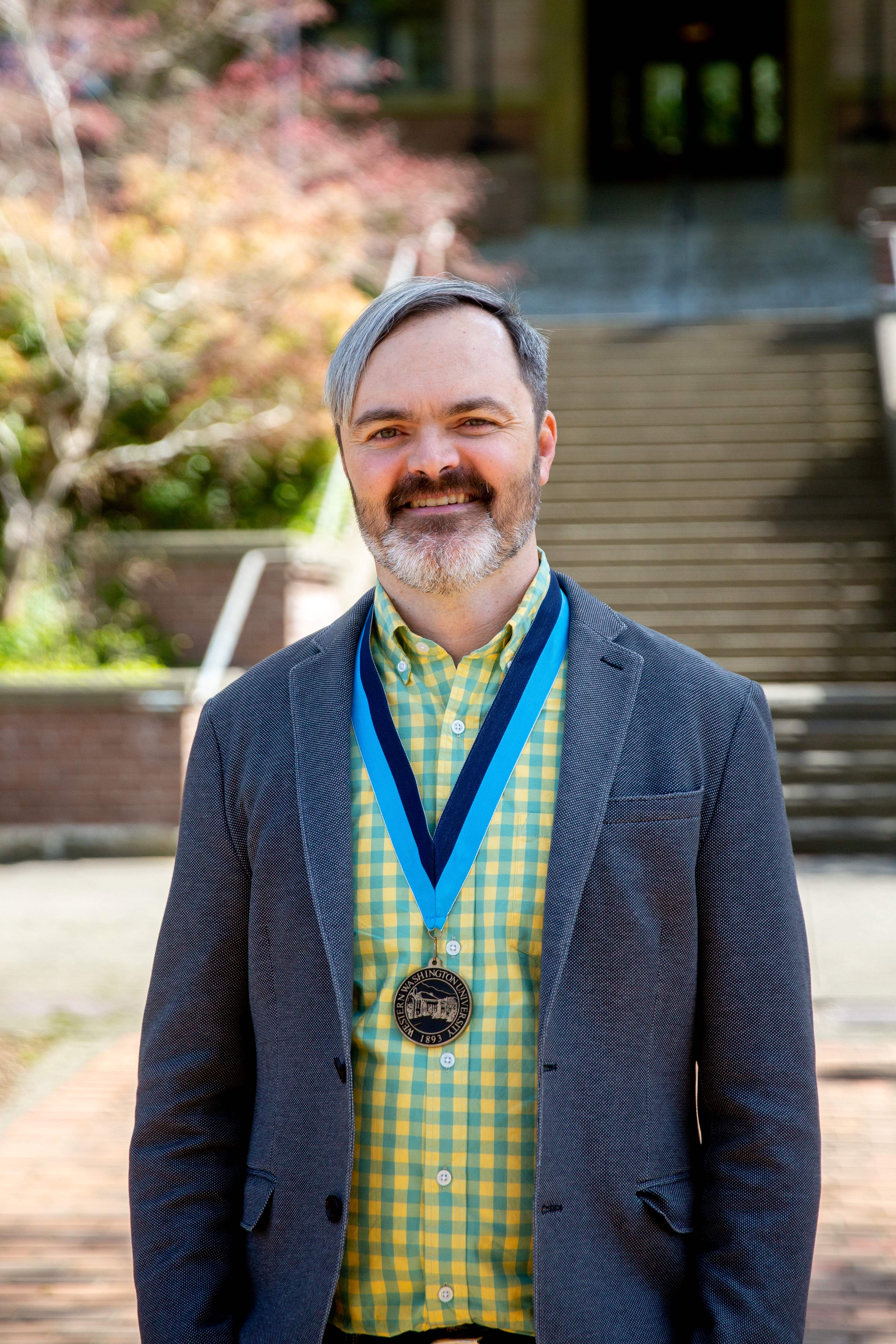 Daniel Chard in a yellow and blue plaid shirt and jacket with a WWU award medallion on a neck ribbon