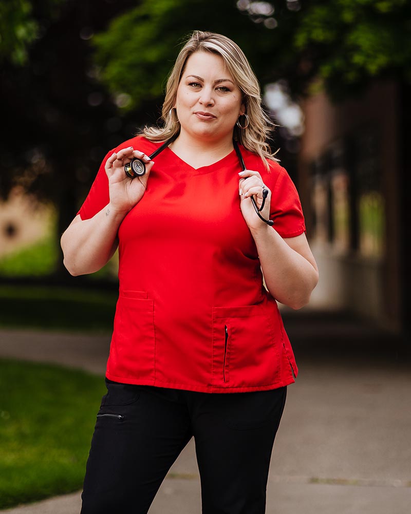 Carisa Blacklock with a stethoscope around her neck, wearing a vibrant red shirt and black pants
