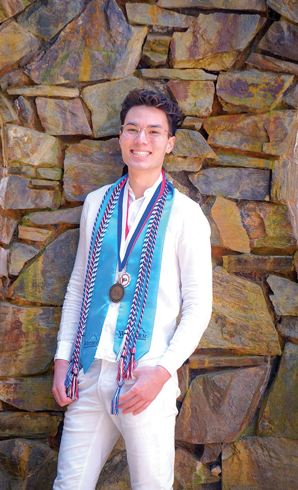 Nate Jo in all white standing in front of a stone facade, wearing a number of sashes and ribbons