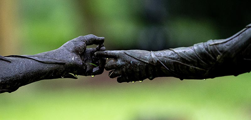 Two hands reaching out, one touching the palm of the other with a single finger. Close up of a bronze scupture.