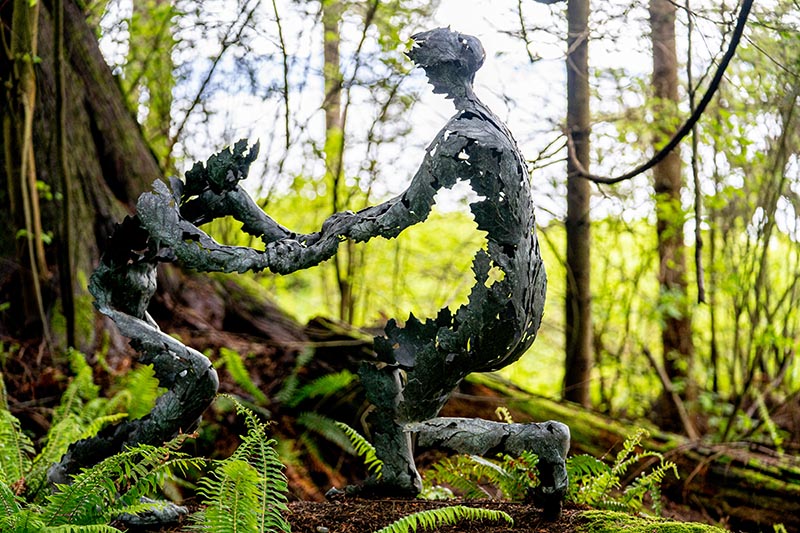 A bronze sculpture of two figures dancing together in the woods. The figures are formed from leaves.