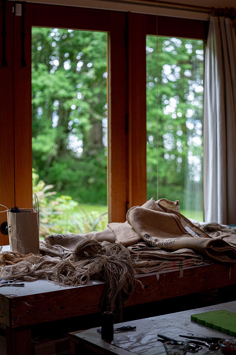 Natural colored textiles stacked on a table next to a door looking out into the woods