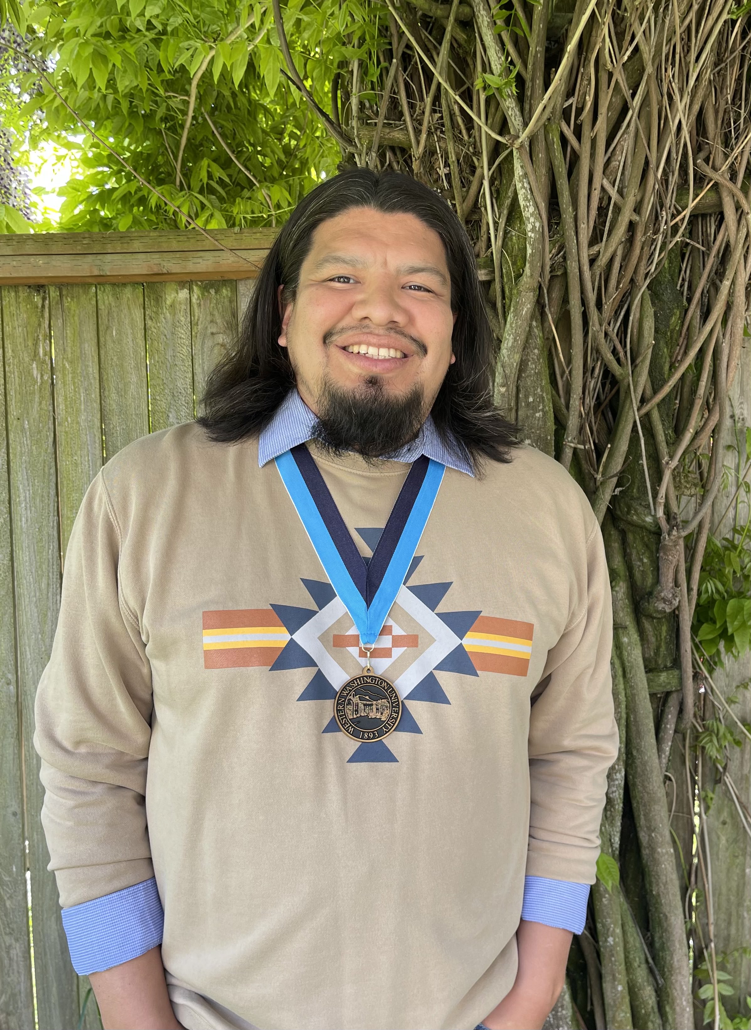 Brandon Joseph smiling broadly wearing a shirt with a colorful native motif and a WWU medallion on a neck ribbon