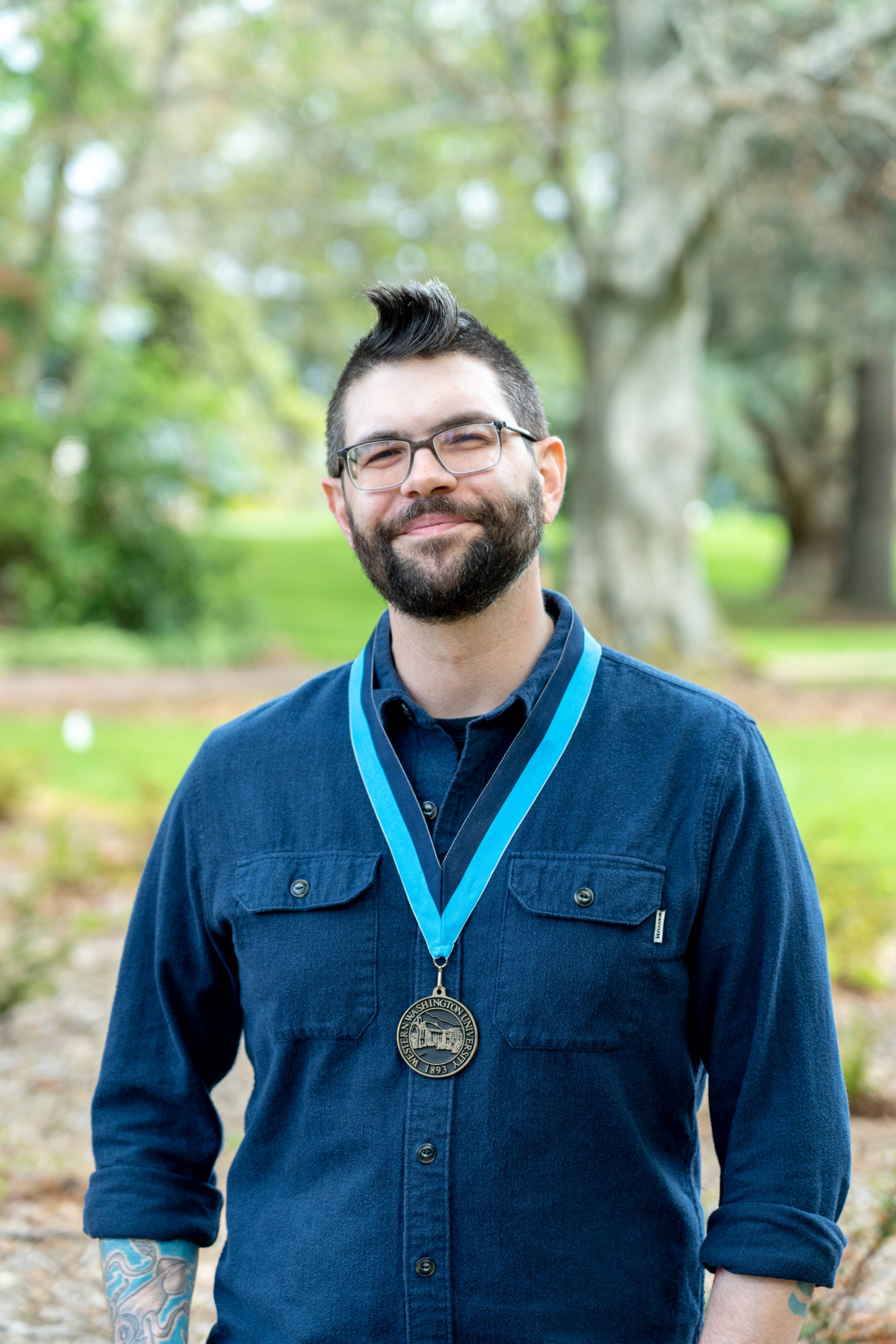 Josh Cerretti smiling warmly wearing a blue shirt and WWU medallion on a neck ribbon