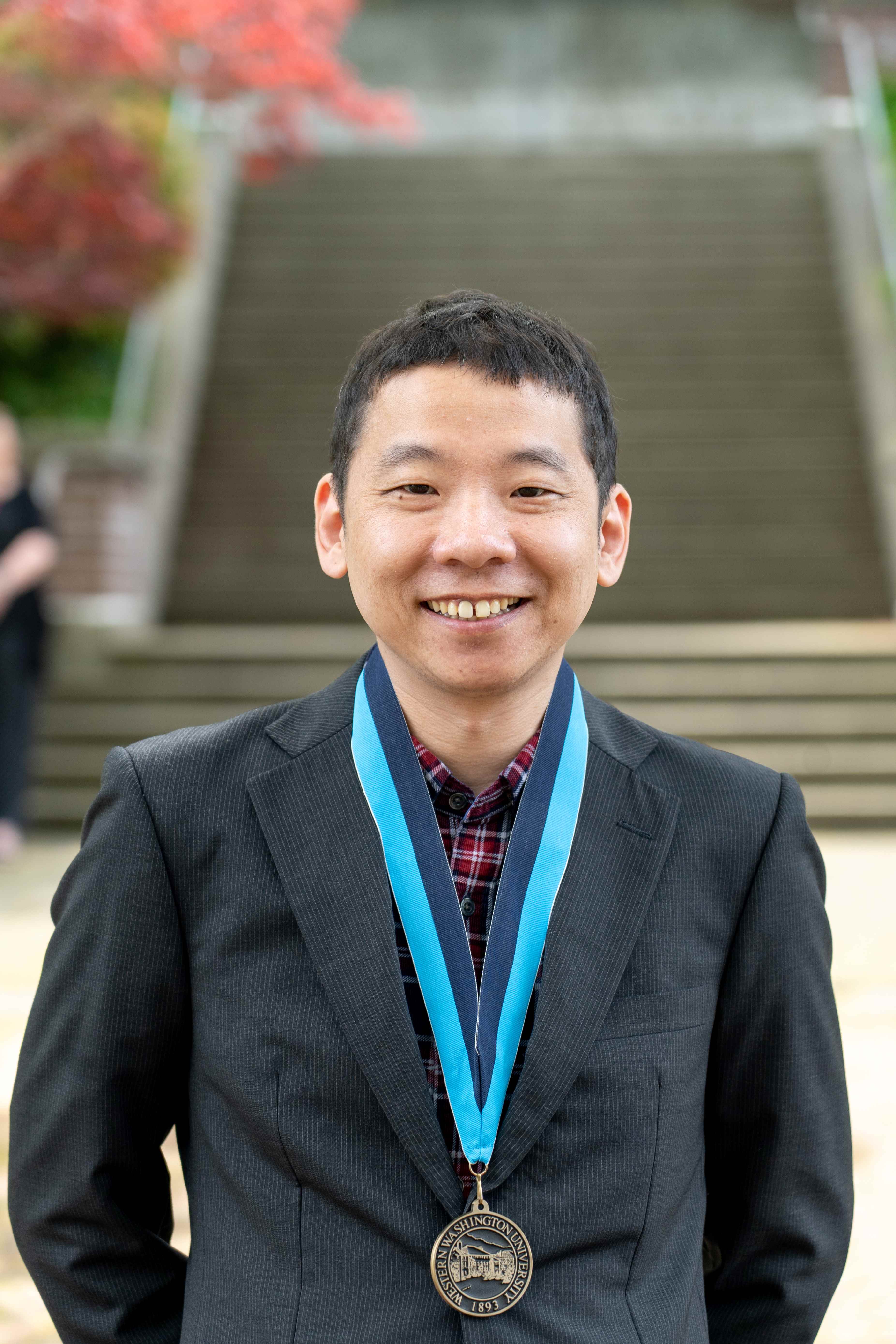 Kimihiro Noguchi smiling proudly in a suit jacket and wearing a WWU medallion on a ribbon.