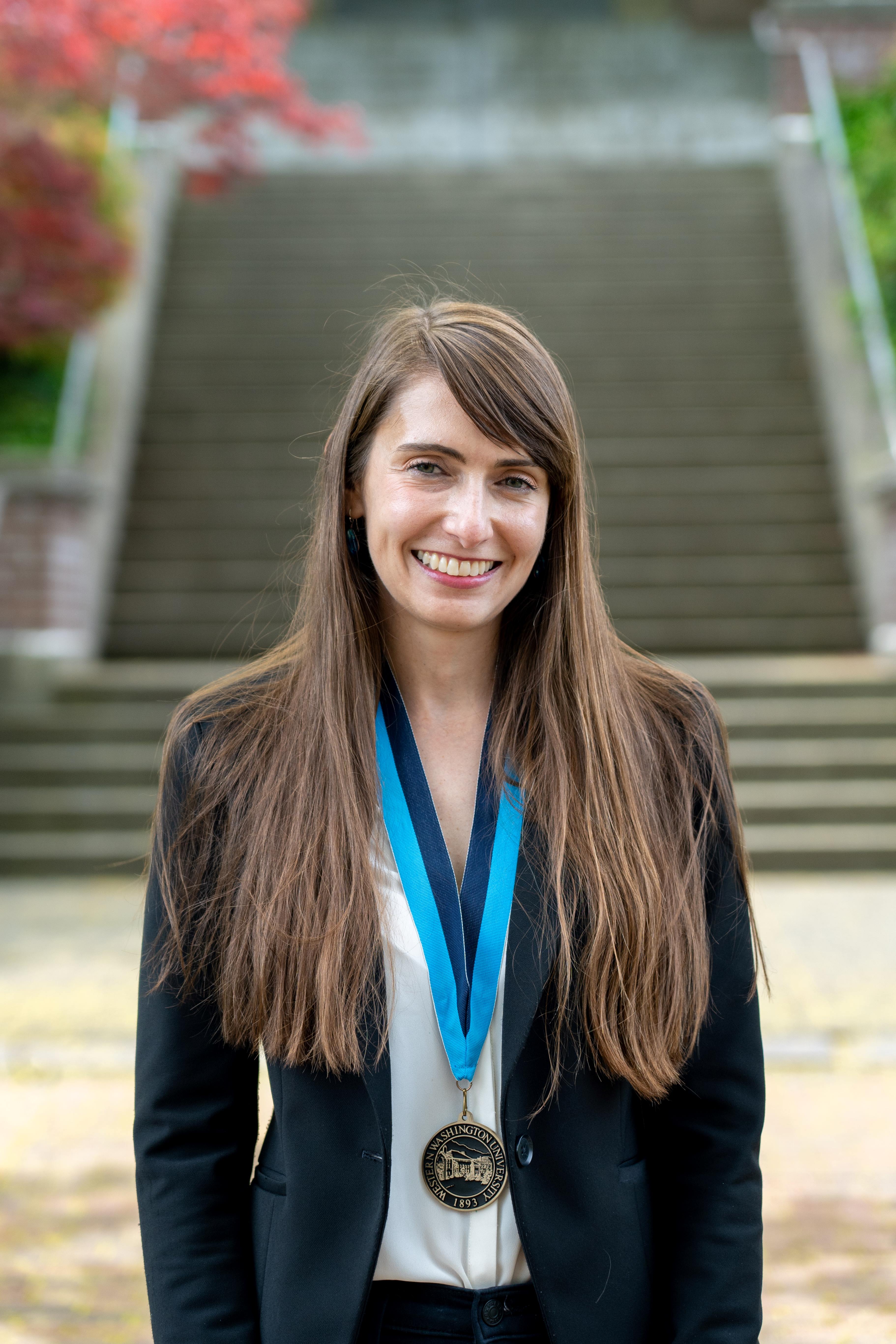 Mariana Smit Vega Garcia smiling sincerely in front of Old Main wearing a WWU award medallion on a neck ribbon