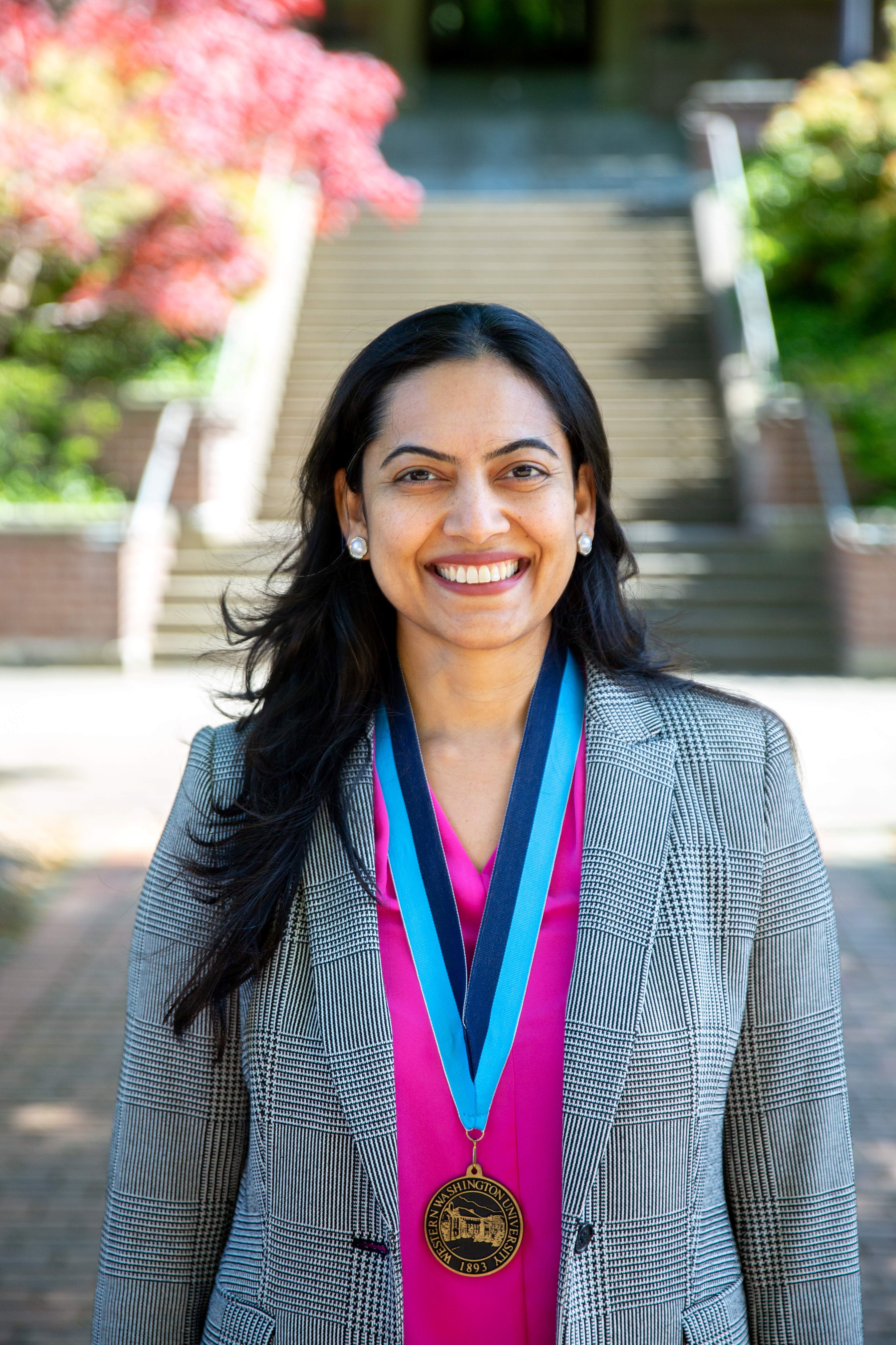 Meg Warren smiling proudly wearing a vivid pink blouse and plaid jacket with a WWU award medallion on a neck ribbon