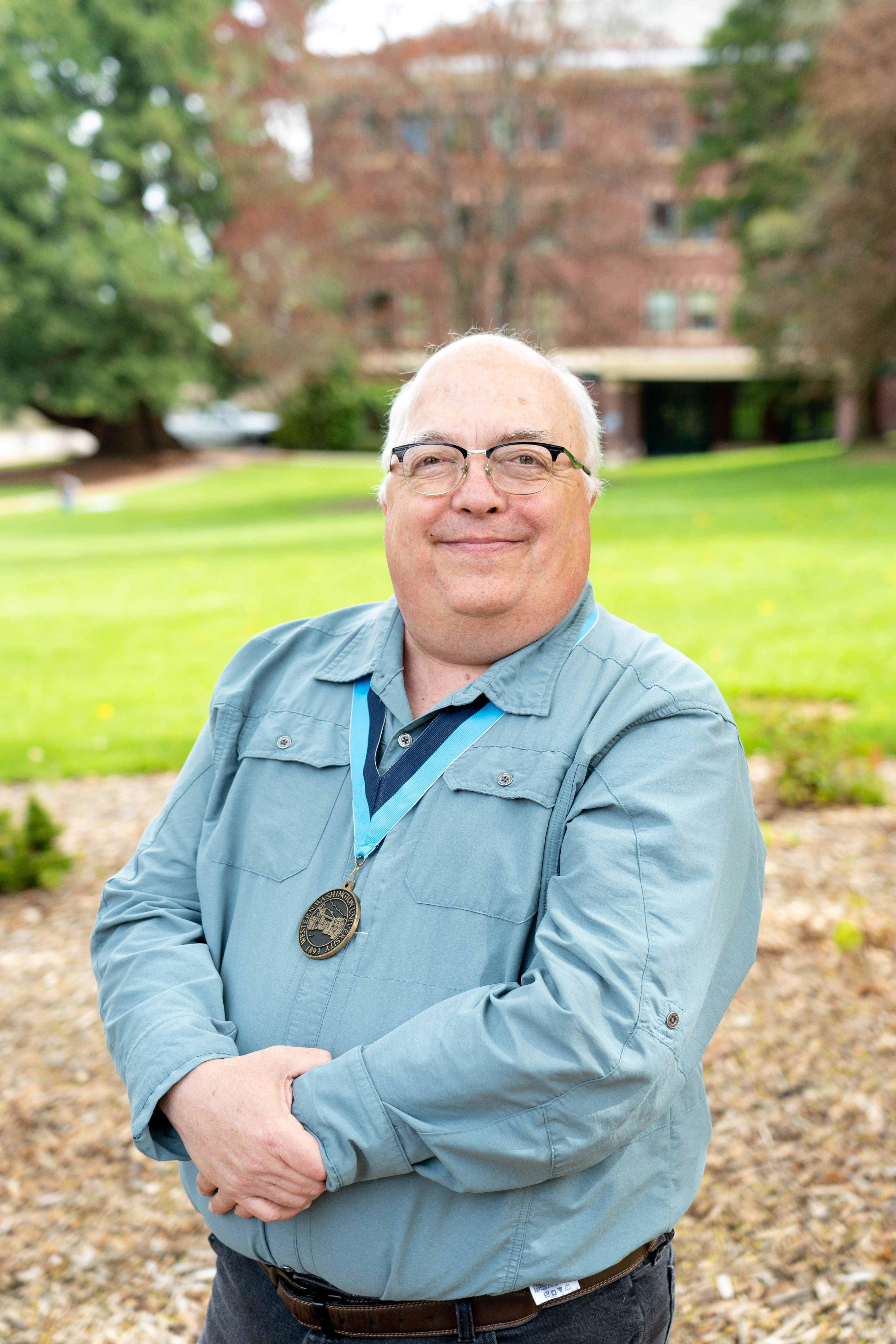 Robert Clark smiles proudly with Edens Hall behind him while wearing a WWU award medallion on a neck ribbon