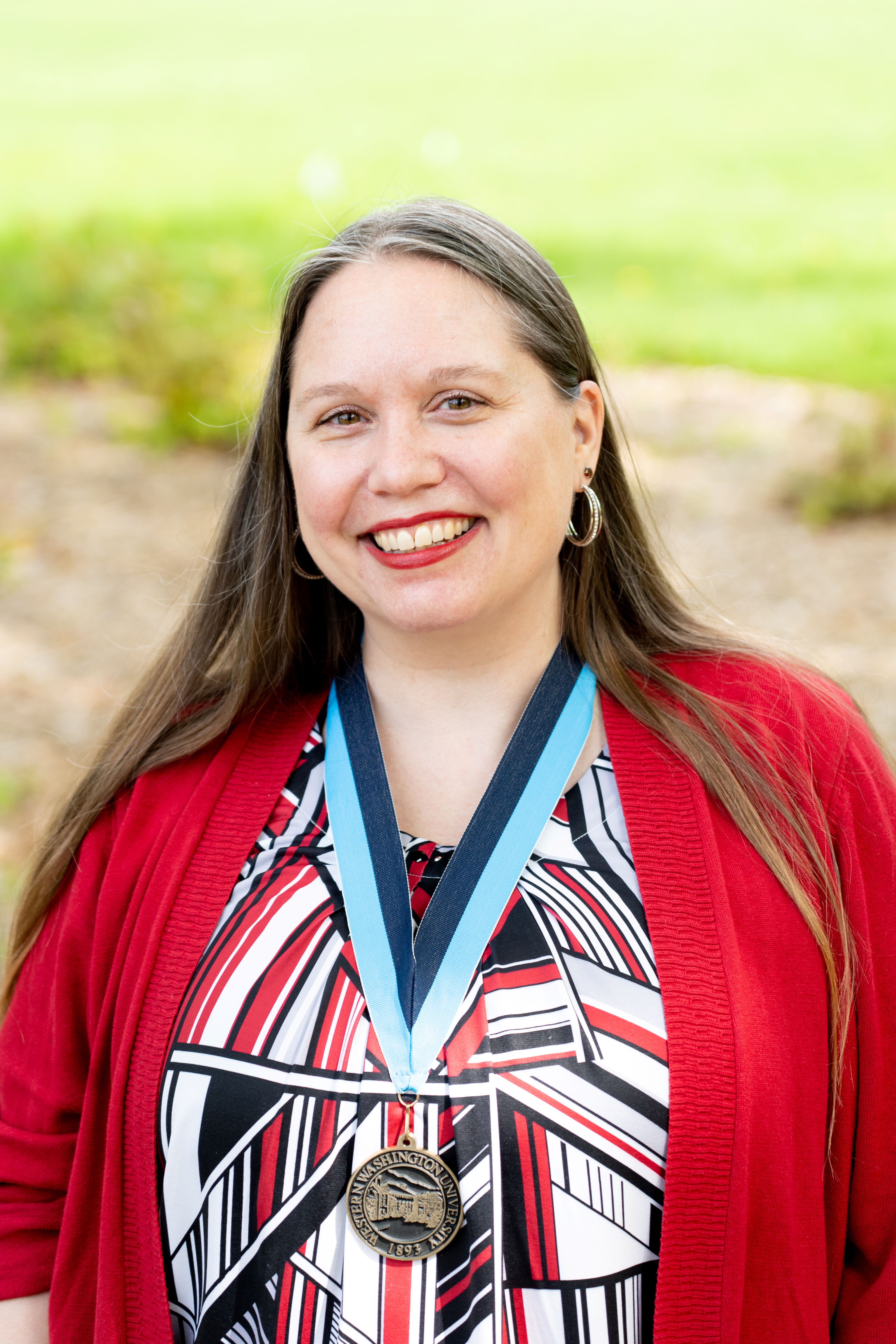 Stephanie Norsby smiling while wearing a bright red cardigan and a WWU award medallion on a neck ribbon