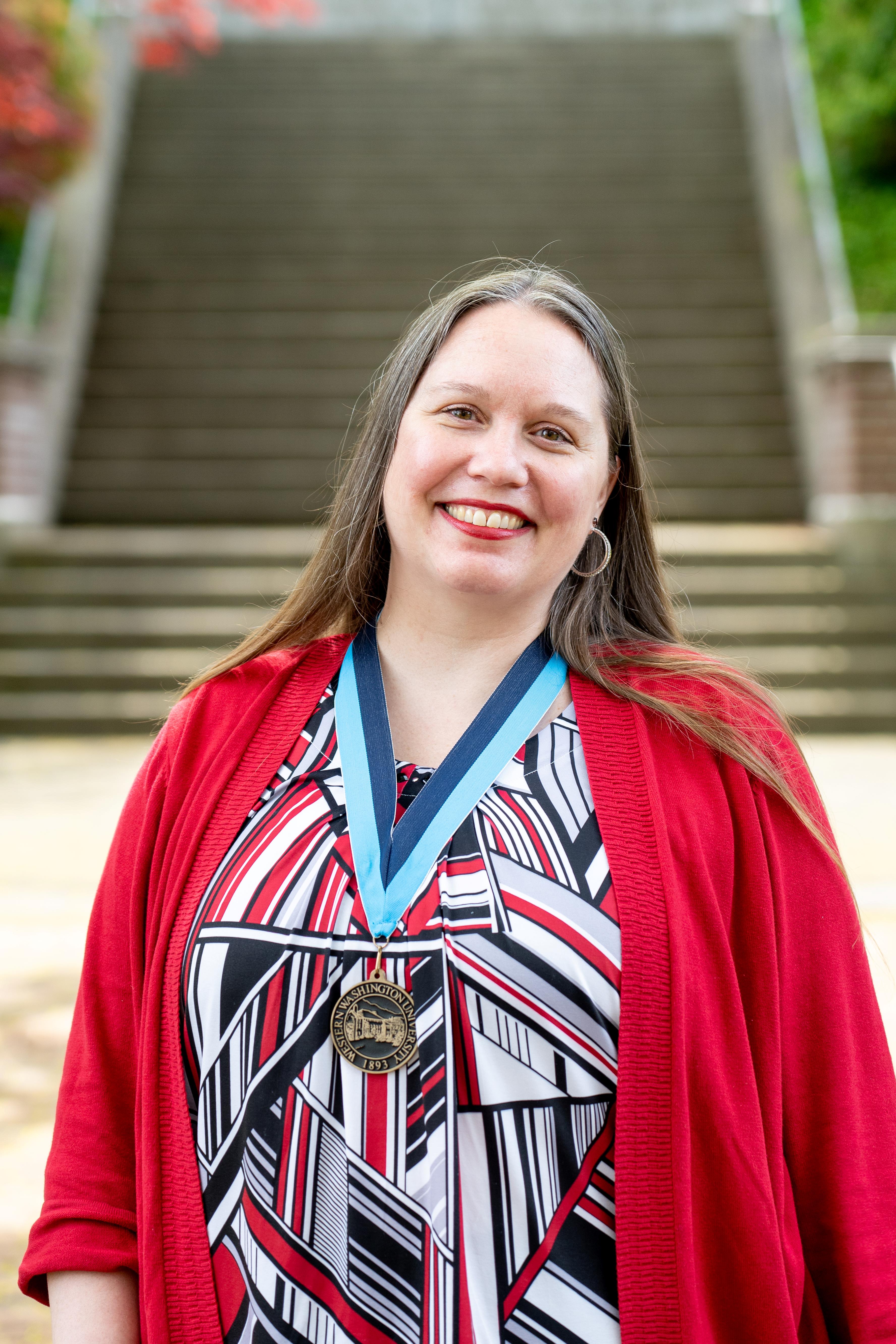 Stephanie Norsby smiling proudly in front of Old Main wearing a WWU award medallion on a neck ribbon