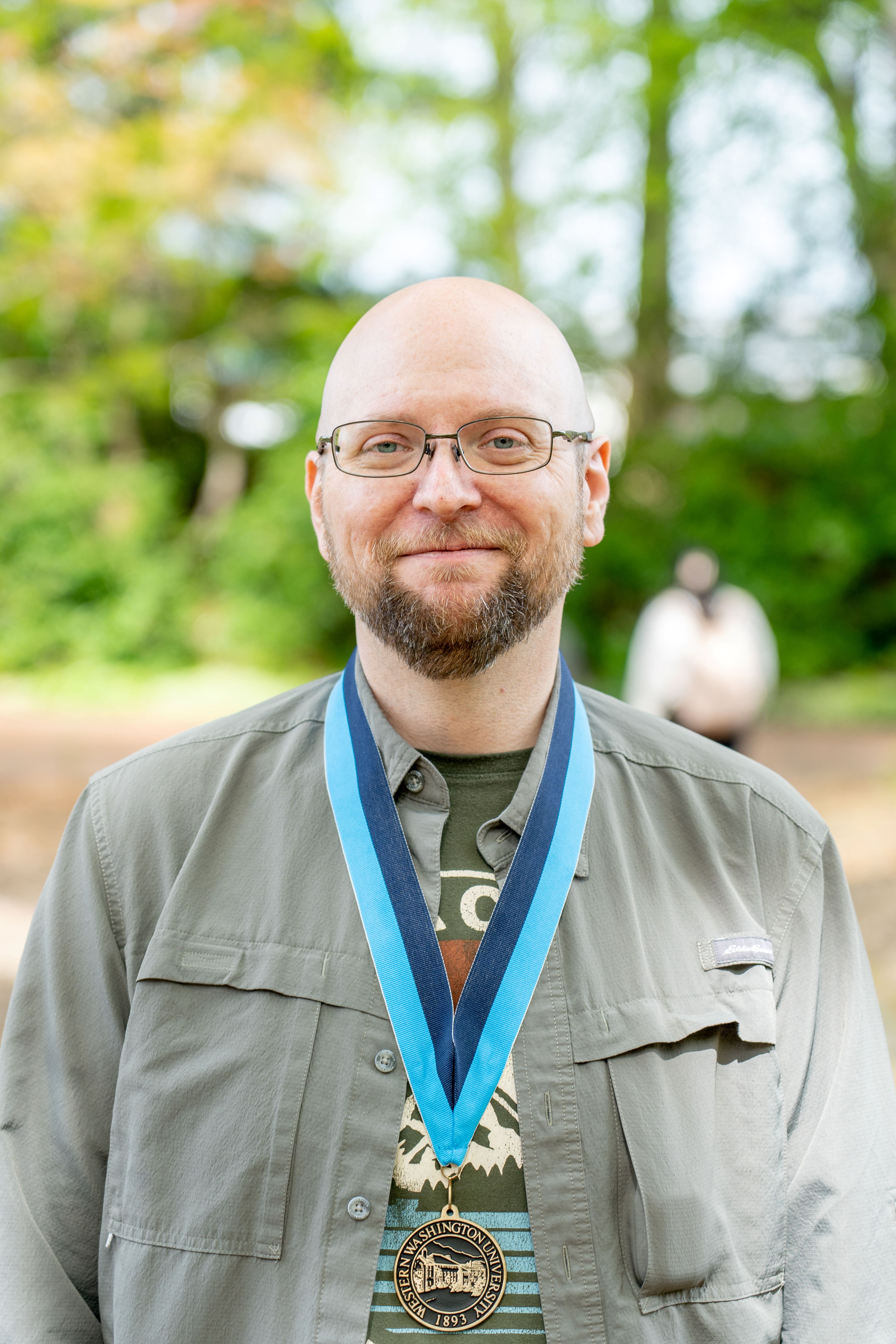 Zach McGrew smiling and wearing a WWU medallion award on a neck ribbon with trees in the background