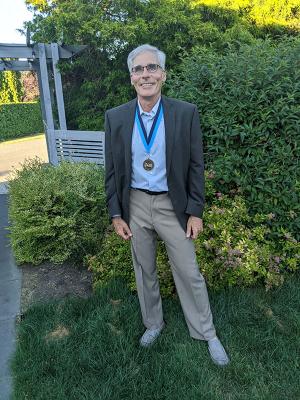 Robert Mitchell of Geology standing in front of green shrubbery wearing his award medallion