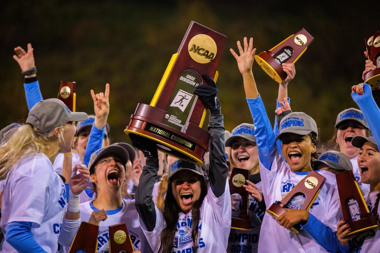 soccer players celebrate their national championship, hoisting large trophies over their heads. 