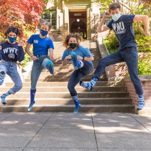 Students wearing masks and WWU shirts and jumping in front of Old Main