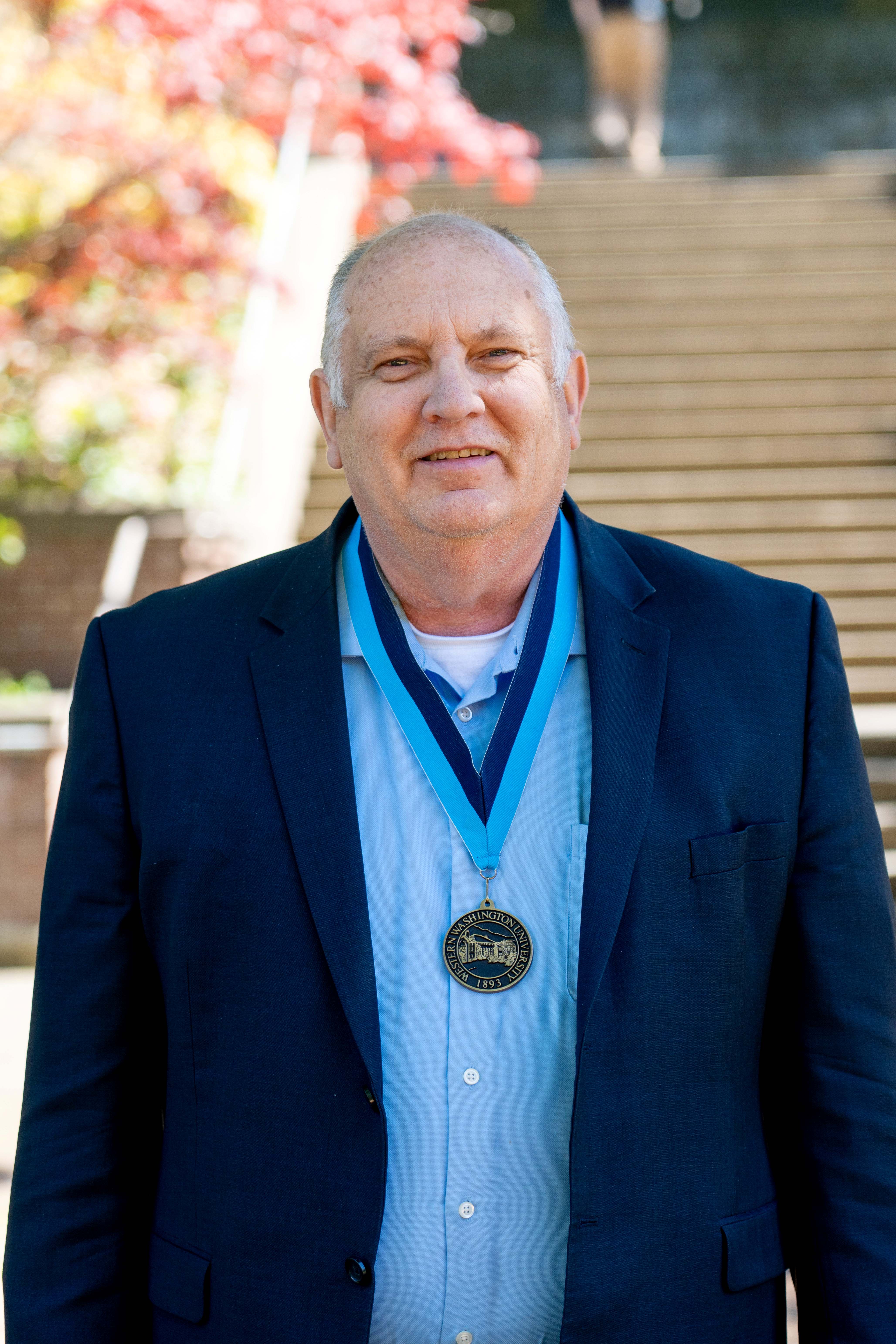 Rick Benner stands in front of the Old Main steps wearing a navy blazer and WWU award medallion