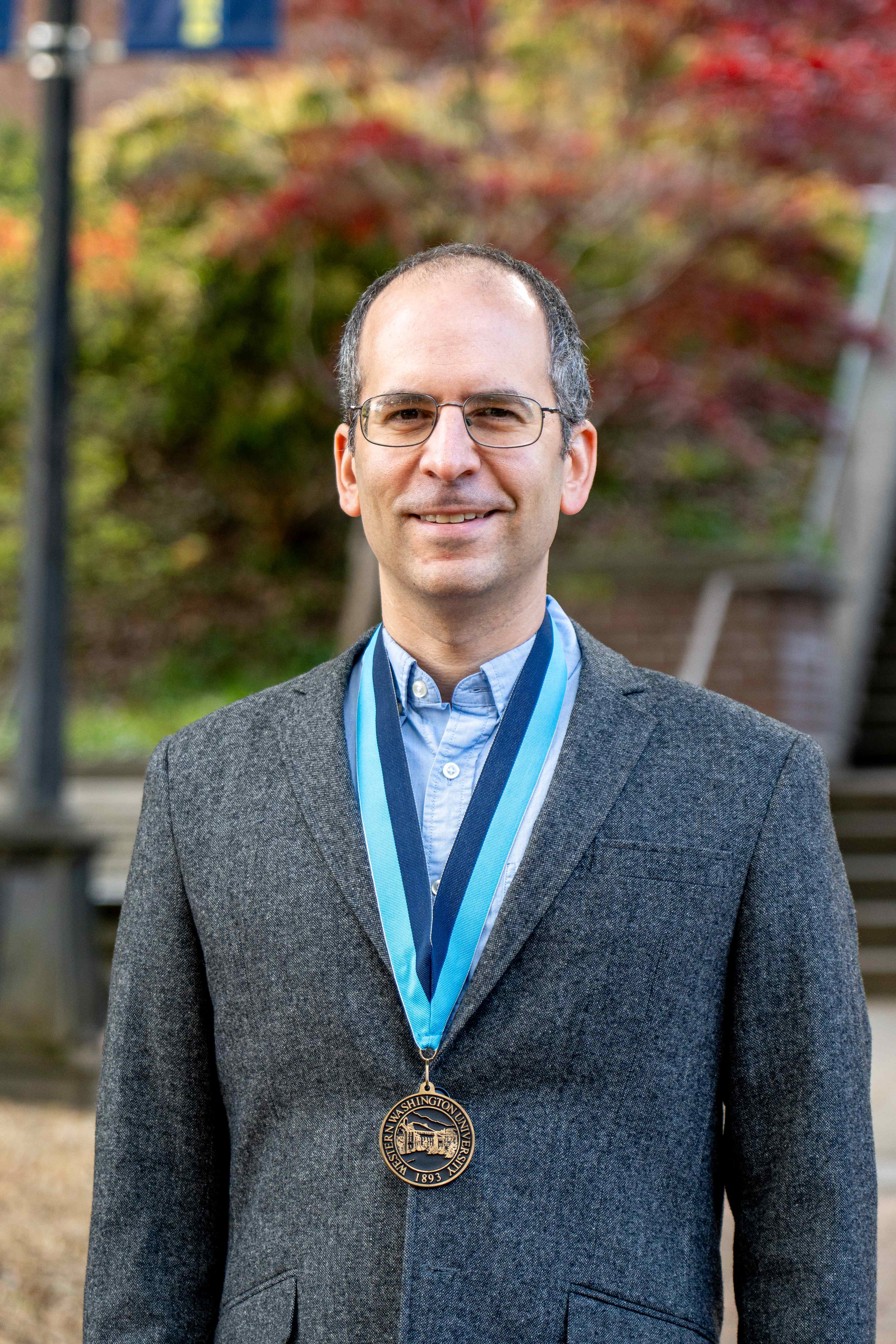 Dr. Robert Berger stands in front of Old Main wearing a tweed blazer and WWU award medallion