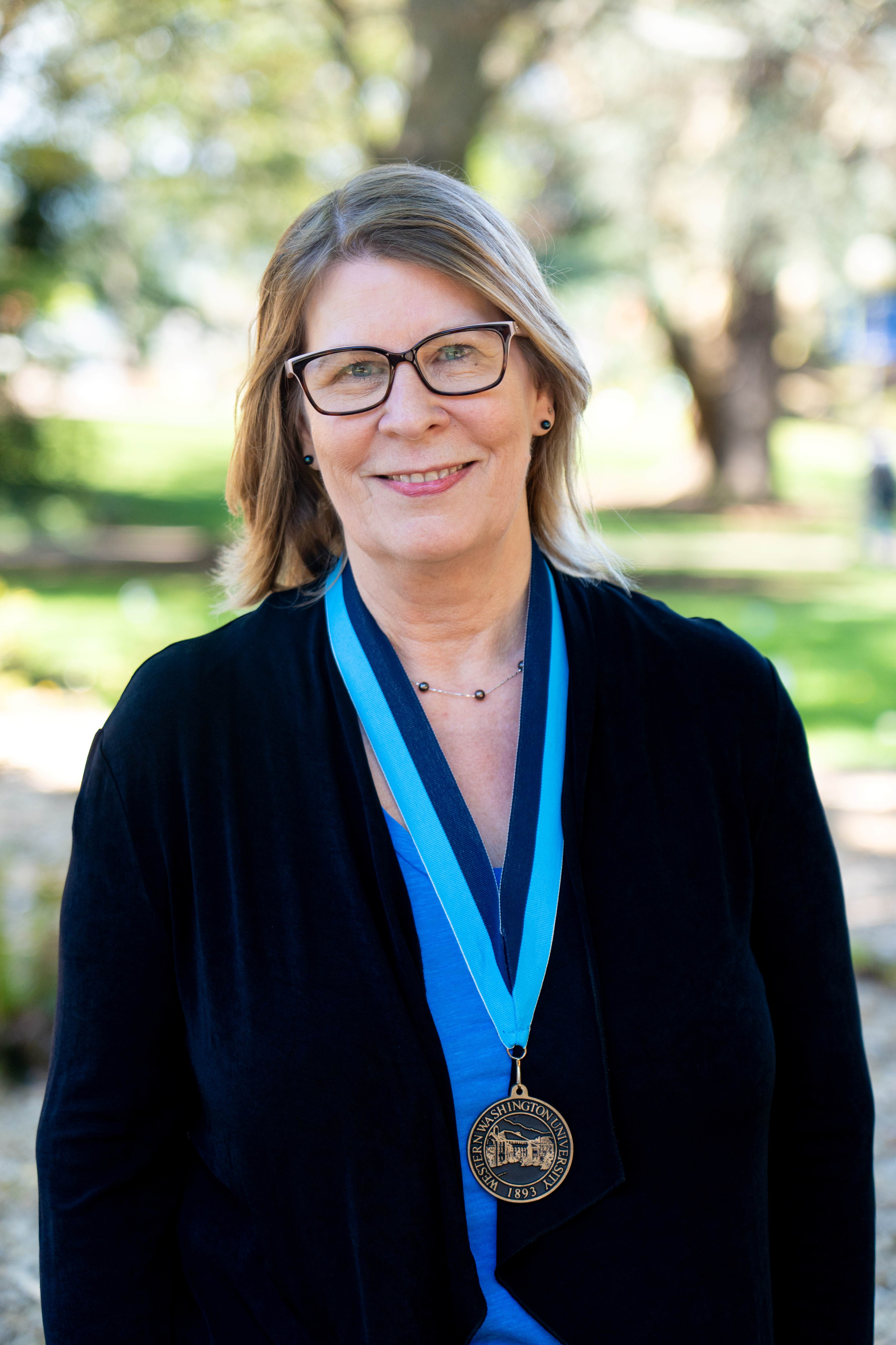 Dr. Kristi Tyran standing on Old Main Lawn wearing a WWU award medallion 