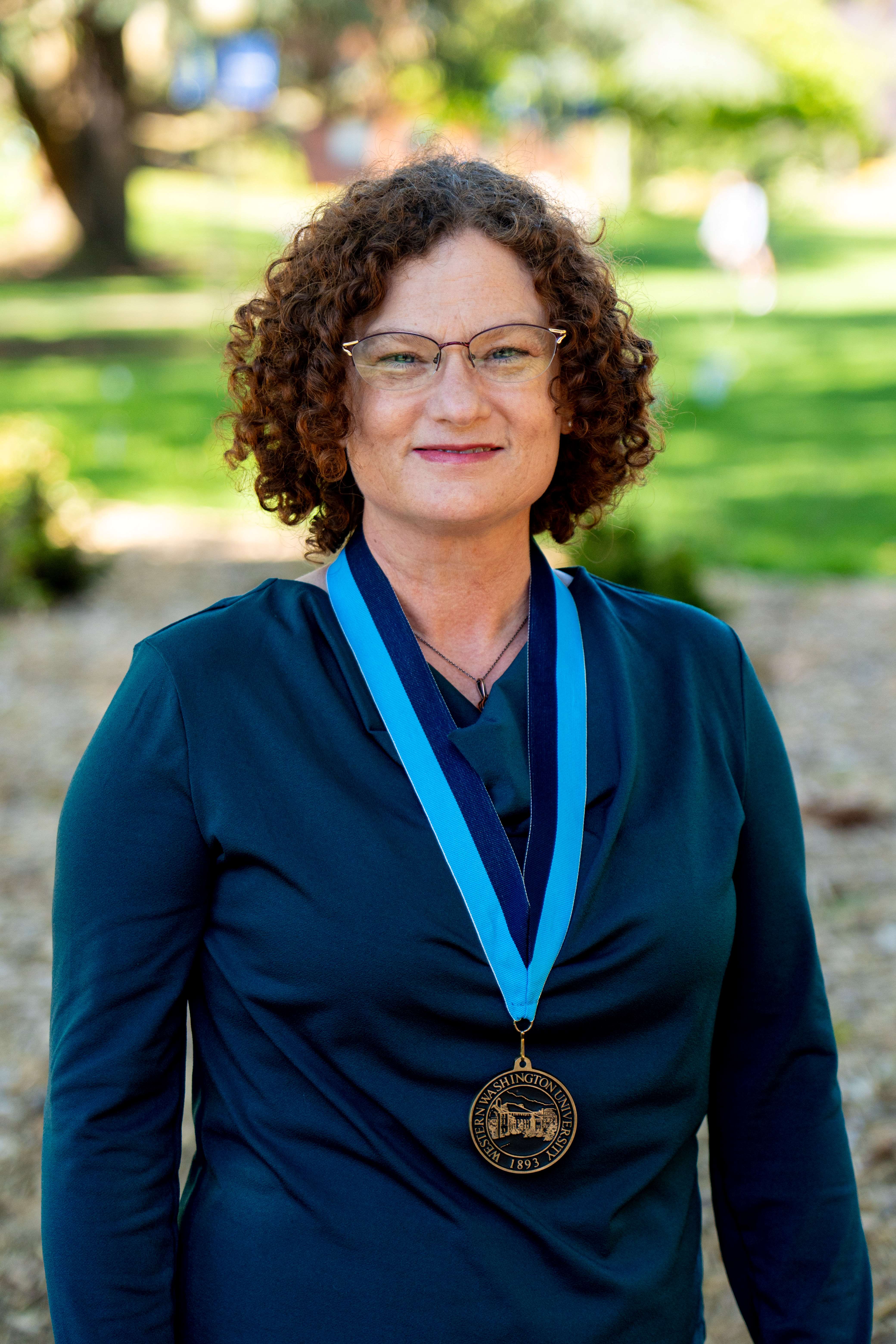 Kimberly Ayre standing with trees in the background and wearing a WWU award medallion