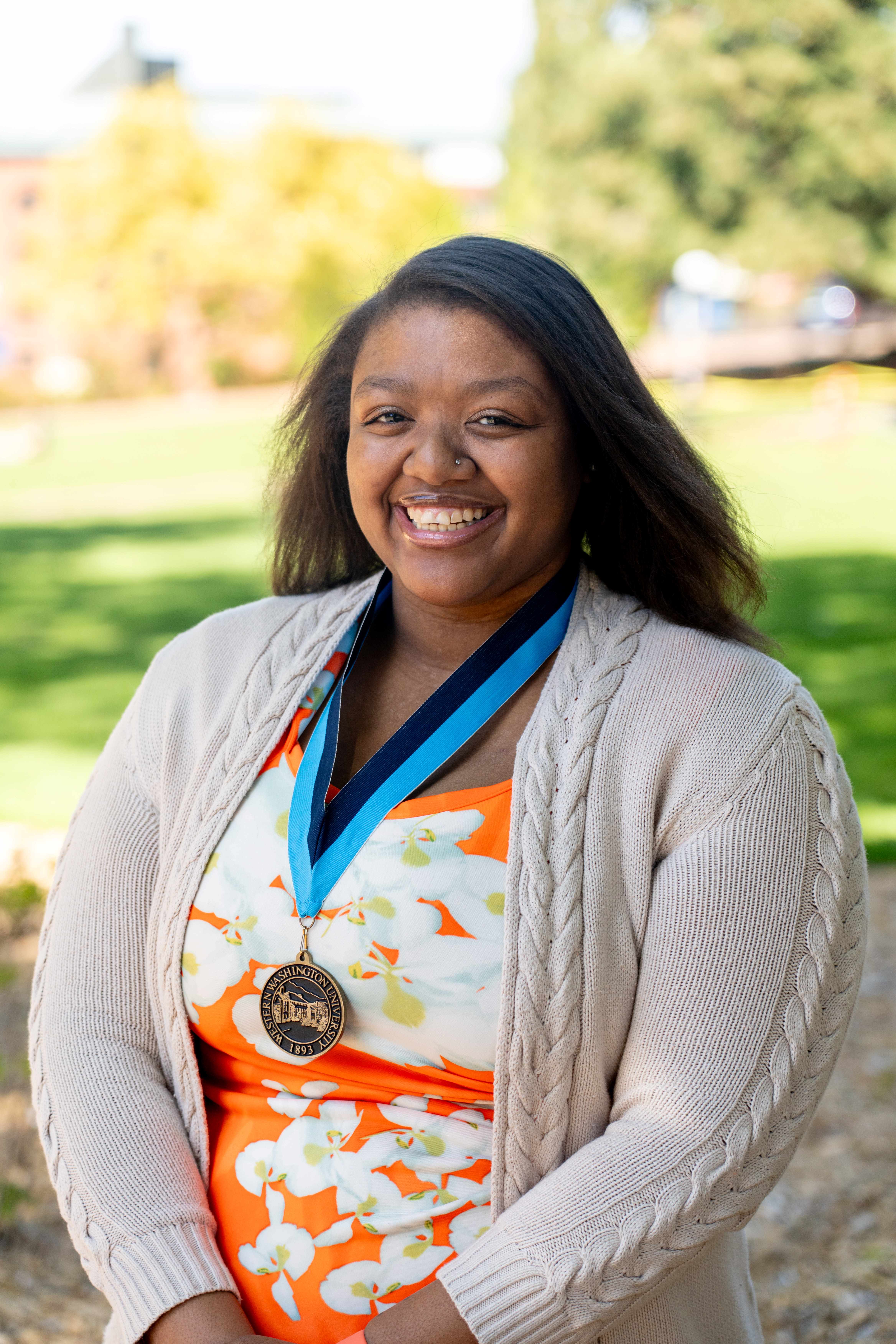 Nia Gipson in front of Old Main wearing an orange floral dress and WWU award medallion