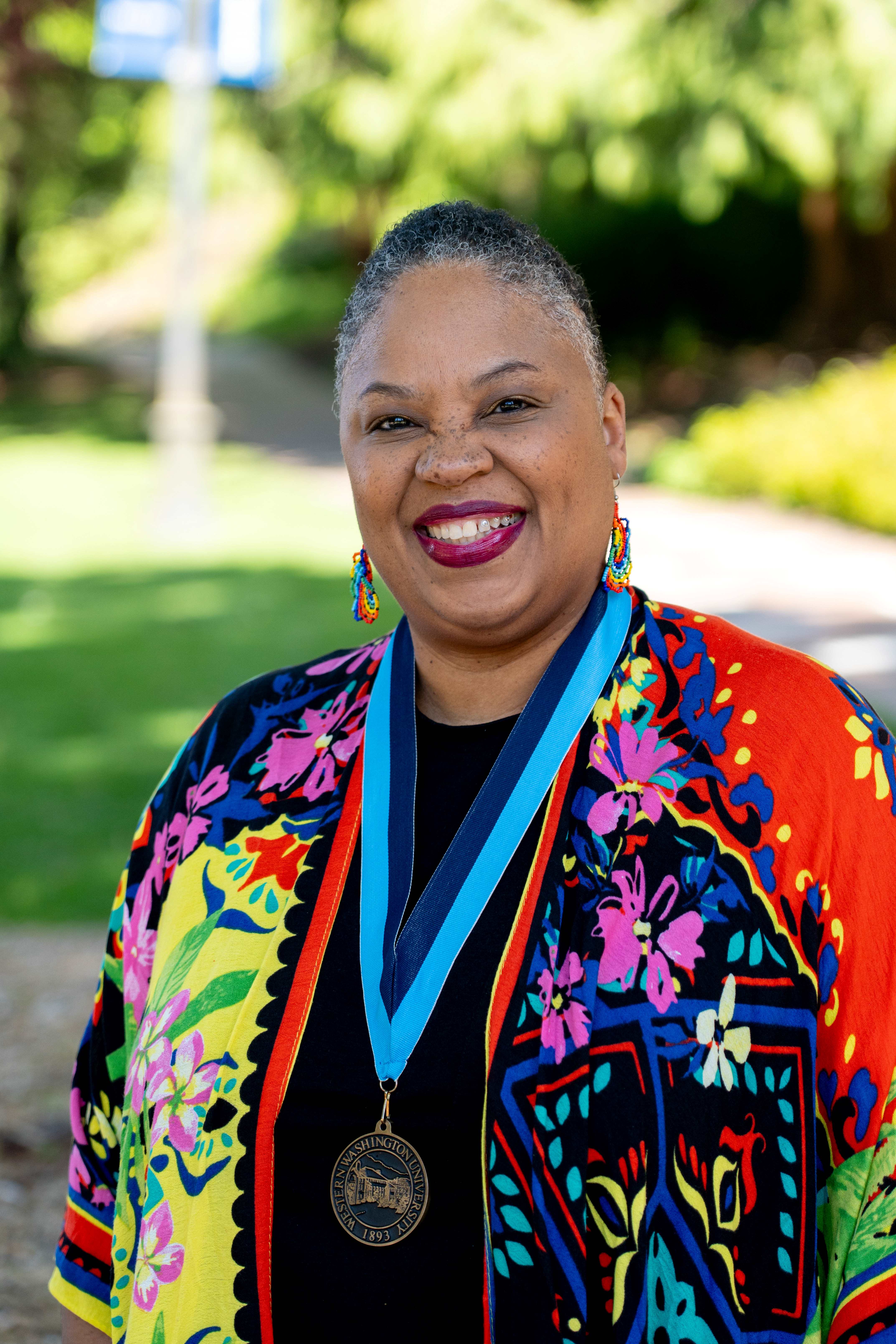 Dr. Tara Perry wearing a vibrant, colorful blouse and a WWU award medallion 