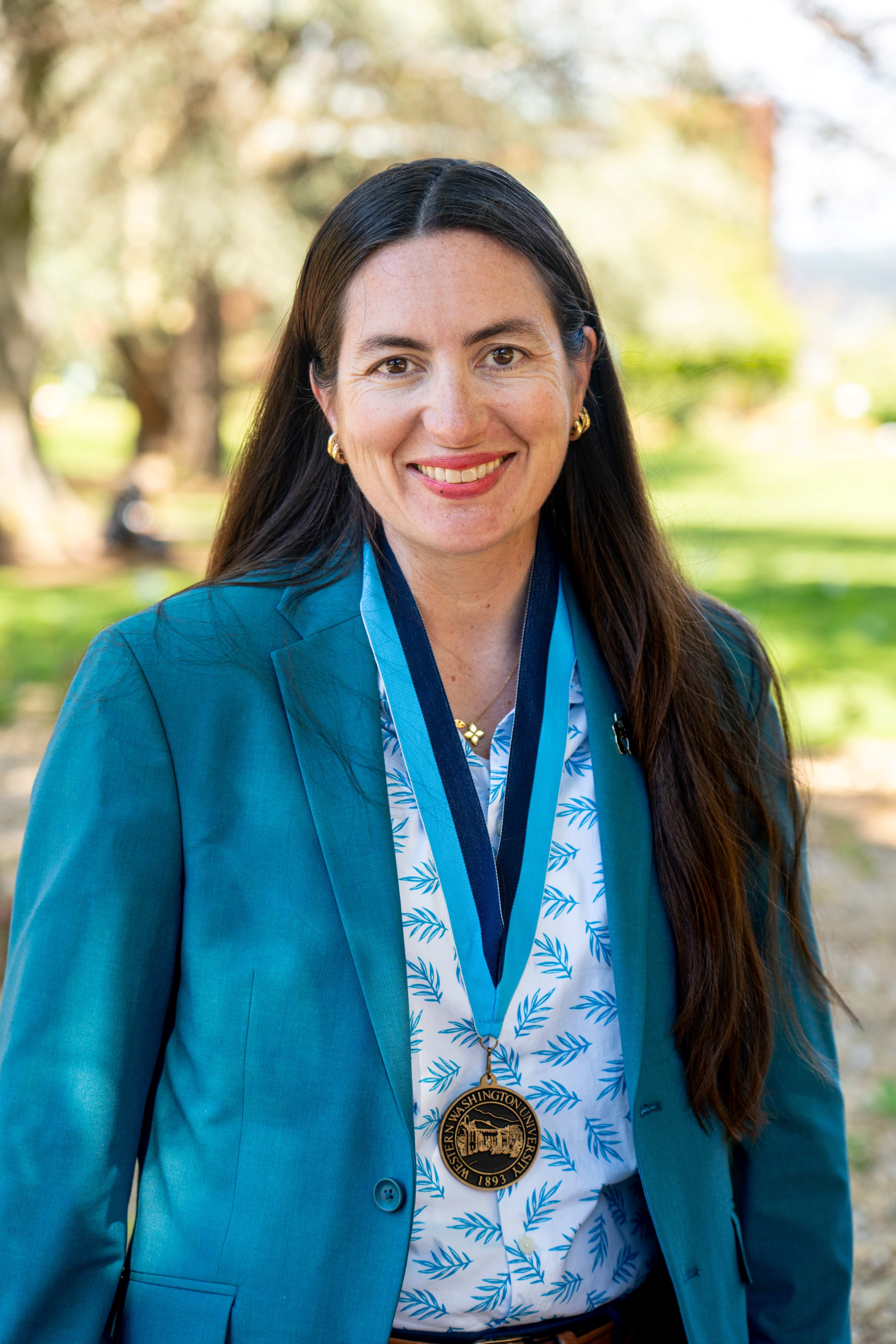 Dr. Tesla Monson wears a vibrant turquoise blazer and a WWU award medallion